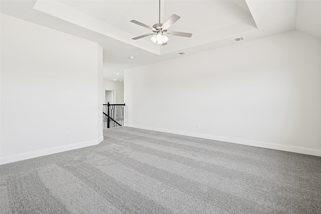 carpeted spare room featuring visible vents, baseboards, a raised ceiling, and a ceiling fan