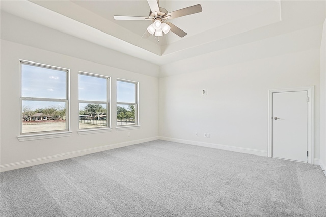 carpeted spare room with baseboards, a tray ceiling, and a ceiling fan