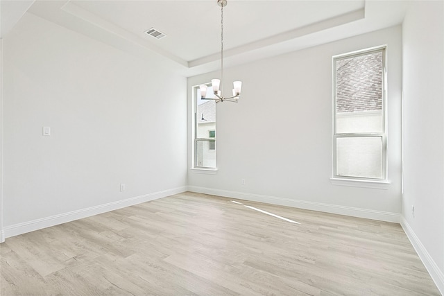 unfurnished room featuring visible vents, baseboards, light wood-type flooring, a tray ceiling, and an inviting chandelier