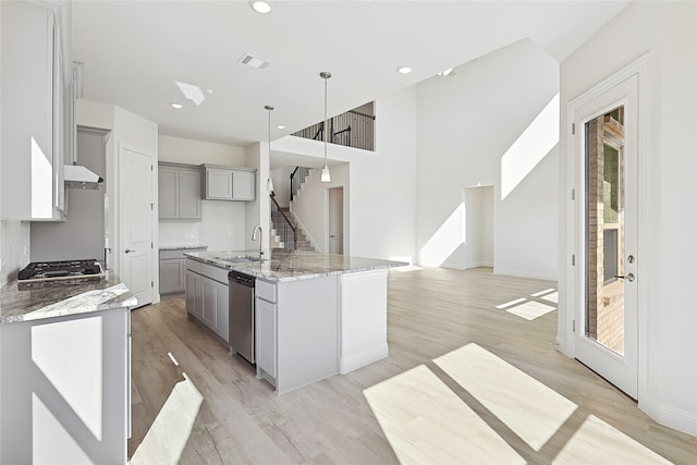 kitchen featuring dishwasher, a kitchen island with sink, hanging light fixtures, gray cabinetry, and light wood-type flooring