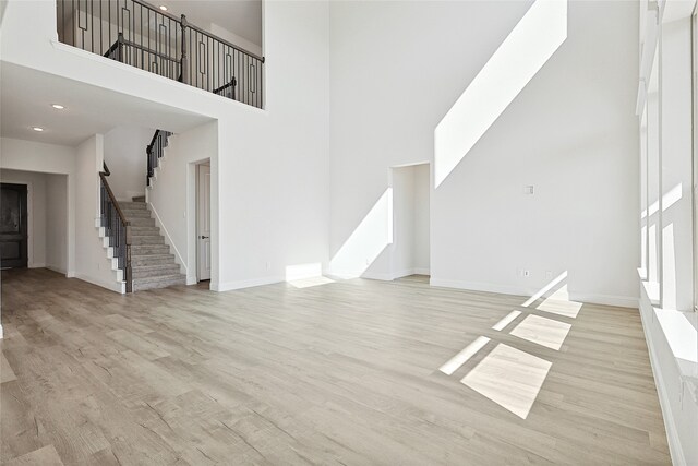 unfurnished living room featuring light hardwood / wood-style floors and a towering ceiling