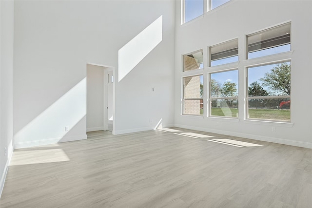 unfurnished living room with a healthy amount of sunlight, a towering ceiling, and light wood-type flooring