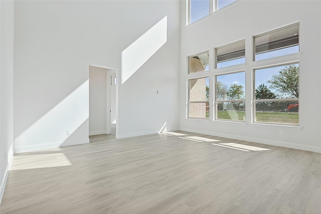 unfurnished living room with baseboards, a towering ceiling, and light wood finished floors