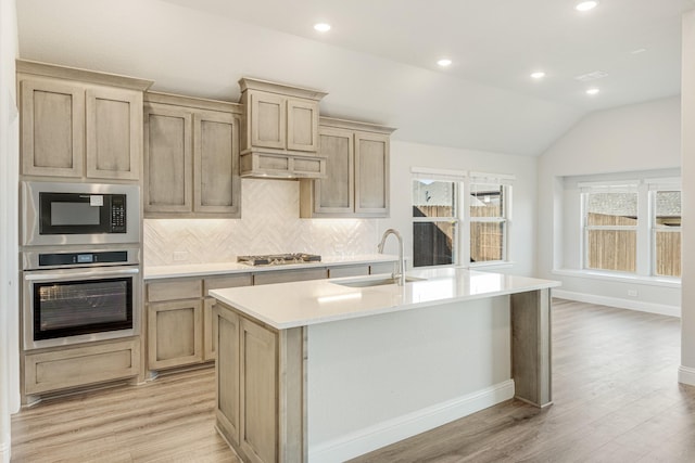 kitchen featuring lofted ceiling, sink, light wood-type flooring, an island with sink, and stainless steel appliances