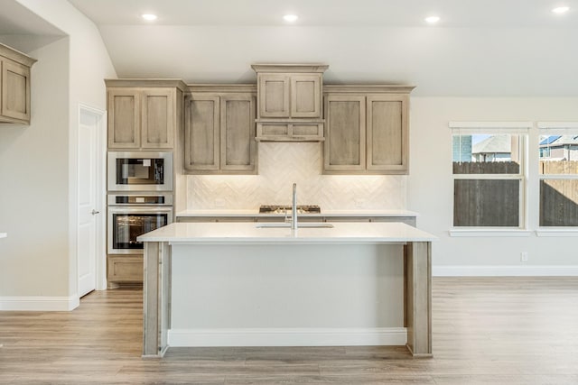 kitchen with light wood-type flooring, stainless steel appliances, and an island with sink