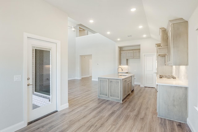 kitchen with decorative backsplash, a kitchen island with sink, sink, light brown cabinets, and light hardwood / wood-style floors