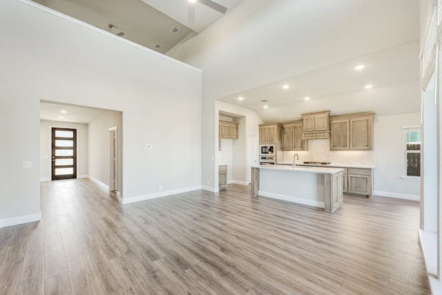 kitchen with ceiling fan, sink, high vaulted ceiling, light hardwood / wood-style floors, and a kitchen island with sink