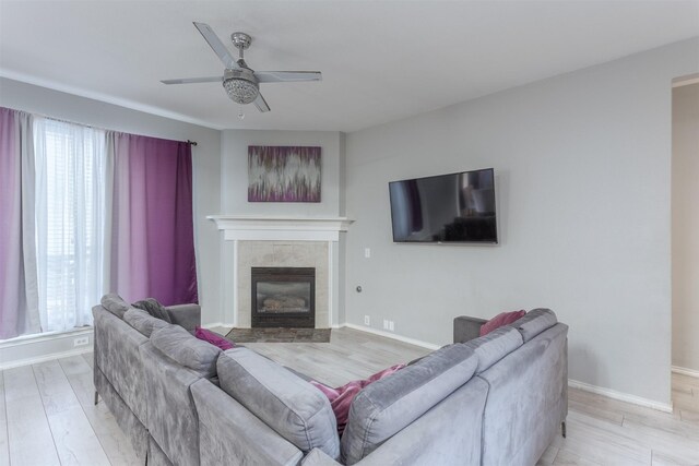 living room featuring a tile fireplace, light wood-type flooring, ceiling fan, and a healthy amount of sunlight