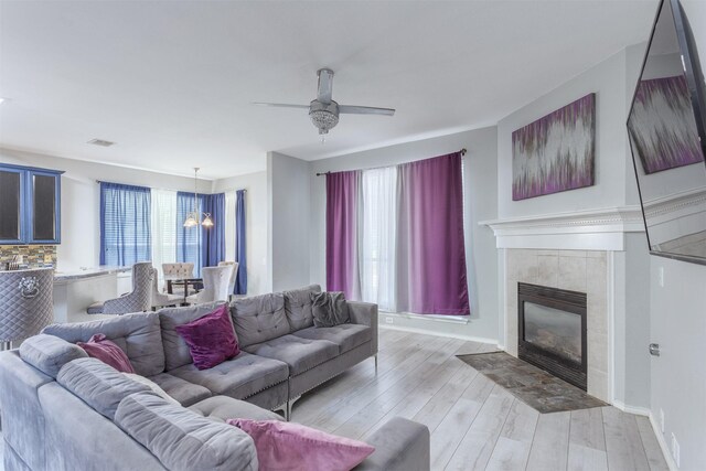 living room with a fireplace, light wood-type flooring, and ceiling fan