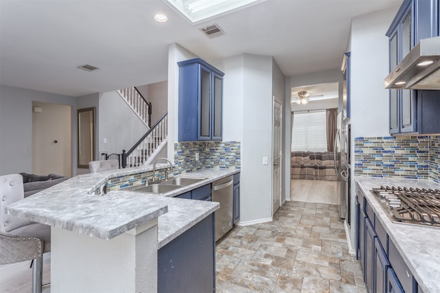 kitchen with stainless steel appliances, wall chimney range hood, light hardwood / wood-style floors, decorative backsplash, and ceiling fan