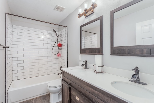 full bathroom featuring double vanity, tiled shower / bath combo, toilet, and hardwood / wood-style floors