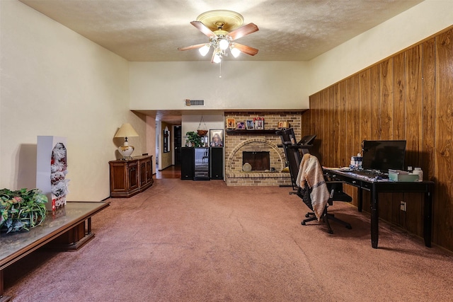 carpeted home office featuring a brick fireplace, a textured ceiling, ceiling fan, and wooden walls