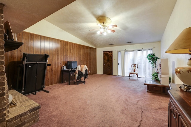 interior space with lofted ceiling, a brick fireplace, wood walls, carpet flooring, and ceiling fan