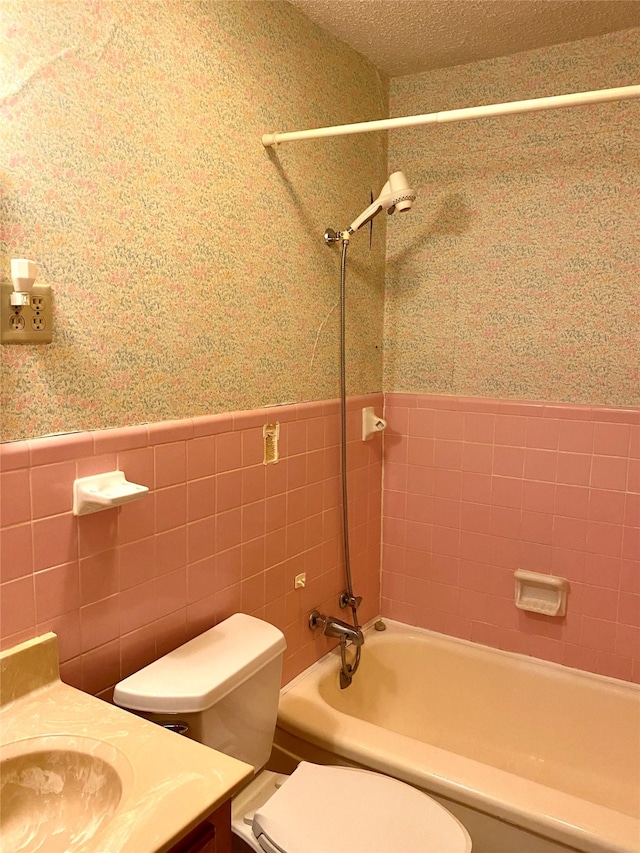 full bathroom featuring vanity, a textured ceiling, tiled shower / bath combo, and toilet