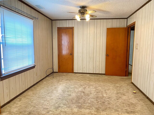 carpeted spare room with wood walls, a textured ceiling, ceiling fan, and ornamental molding