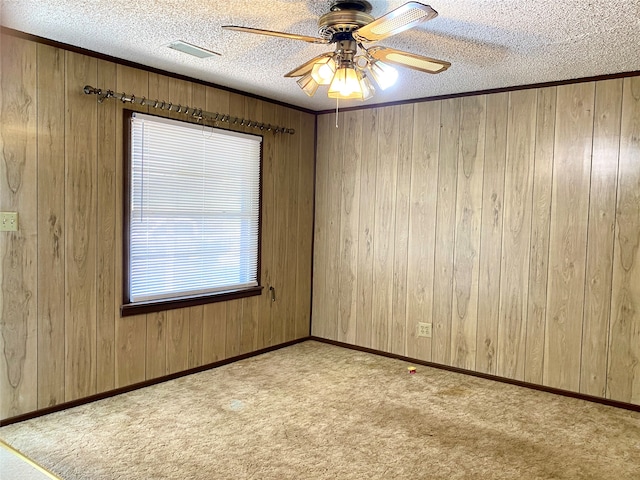 carpeted spare room with wood walls, a textured ceiling, and ceiling fan