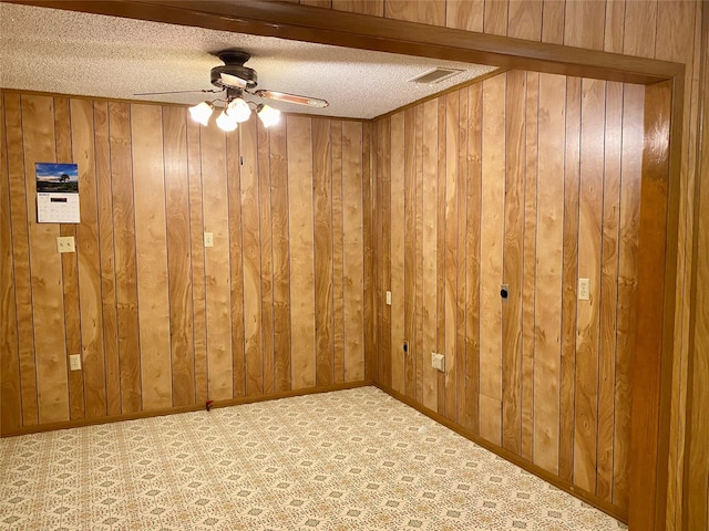 spare room with ceiling fan, a textured ceiling, wooden walls, visible vents, and baseboards