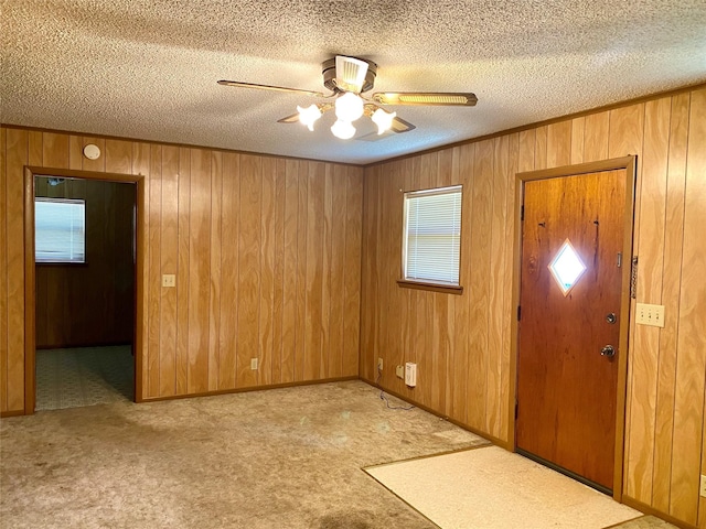 entryway with wood walls, light carpet, ceiling fan, and a textured ceiling