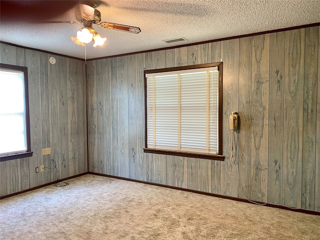 carpeted spare room featuring wooden walls, a textured ceiling, and ceiling fan