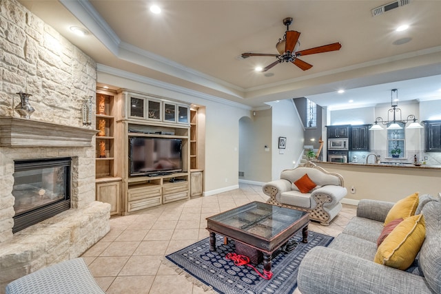 living room with light tile patterned floors, a stone fireplace, crown molding, and ceiling fan