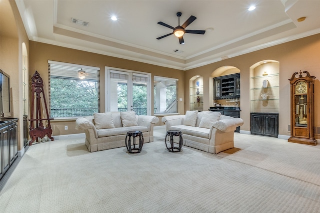 carpeted living room featuring a raised ceiling, built in features, ornamental molding, and ceiling fan