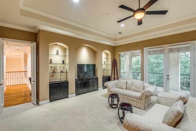 living room featuring ceiling fan, built in shelves, ornamental molding, a raised ceiling, and light hardwood / wood-style floors