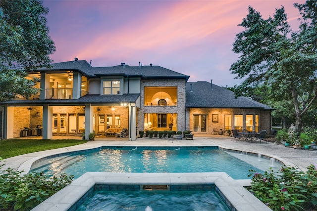 back house at dusk featuring a patio, a balcony, and a pool with hot tub