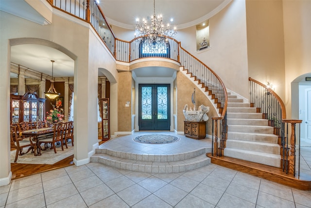 foyer entrance with ornamental molding, a towering ceiling, light wood-type flooring, and a chandelier