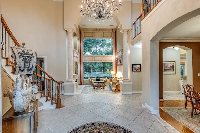 entrance foyer featuring a chandelier, a high ceiling, ornamental molding, ornate columns, and light hardwood / wood-style flooring