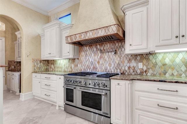 kitchen with dark stone counters, decorative backsplash, crown molding, double oven range, and custom range hood