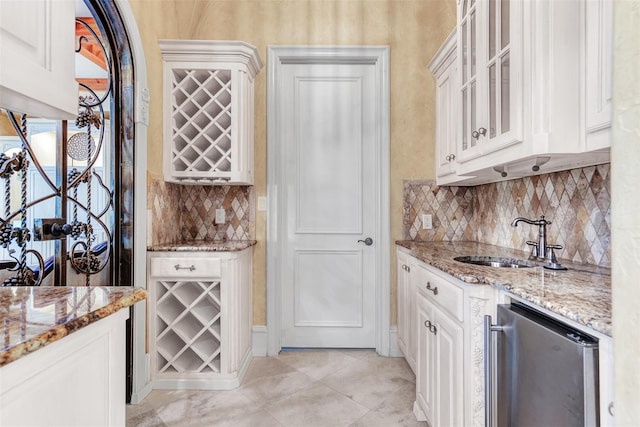 kitchen with white cabinetry, tasteful backsplash, sink, light stone counters, and light tile patterned floors