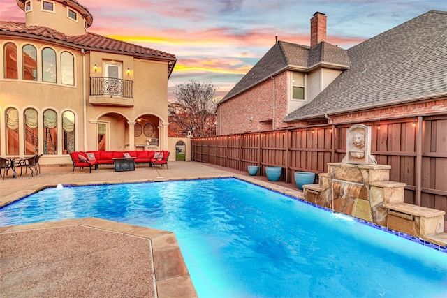 pool at dusk featuring a patio, pool water feature, and outdoor lounge area