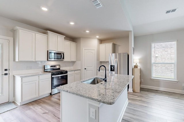 kitchen with sink, white cabinetry, light stone counters, appliances with stainless steel finishes, and a kitchen island with sink