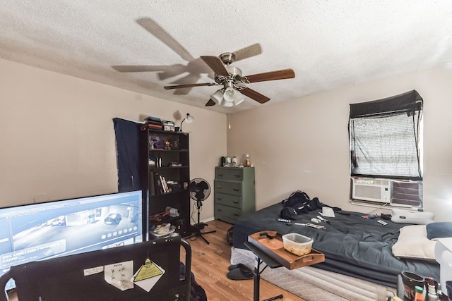 bedroom featuring cooling unit, light wood-type flooring, ceiling fan, and a textured ceiling