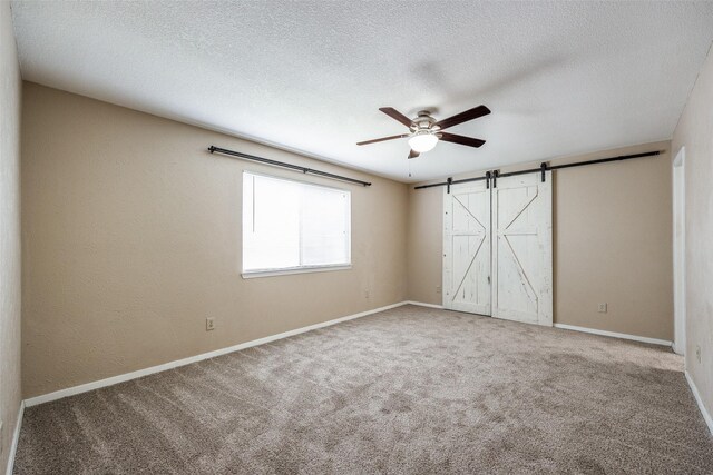 spare room with a textured ceiling, a barn door, carpet flooring, and ceiling fan