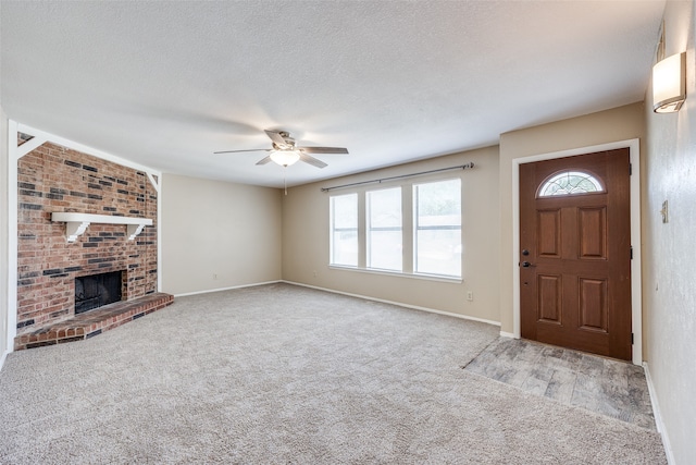 carpeted foyer entrance featuring a textured ceiling, a brick fireplace, and ceiling fan