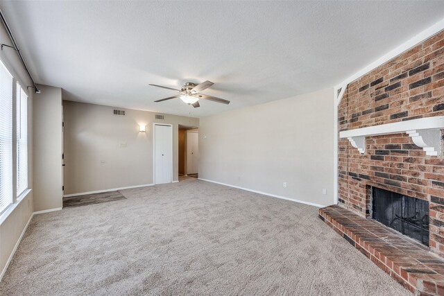 unfurnished living room with a textured ceiling, carpet floors, a brick fireplace, and ceiling fan