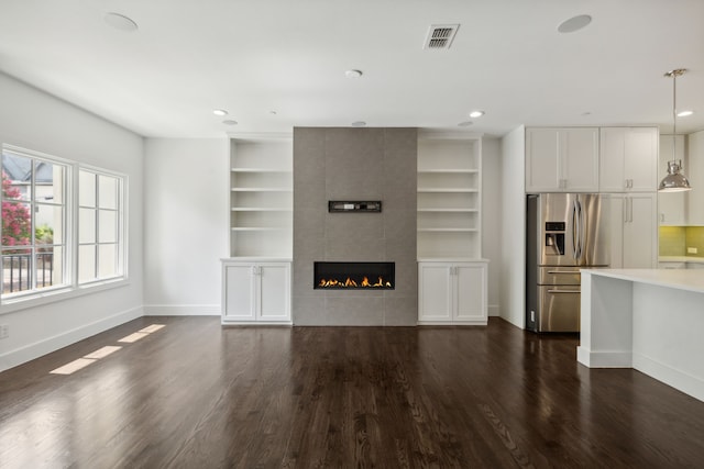 unfurnished living room featuring built in features, a tile fireplace, and hardwood / wood-style floors