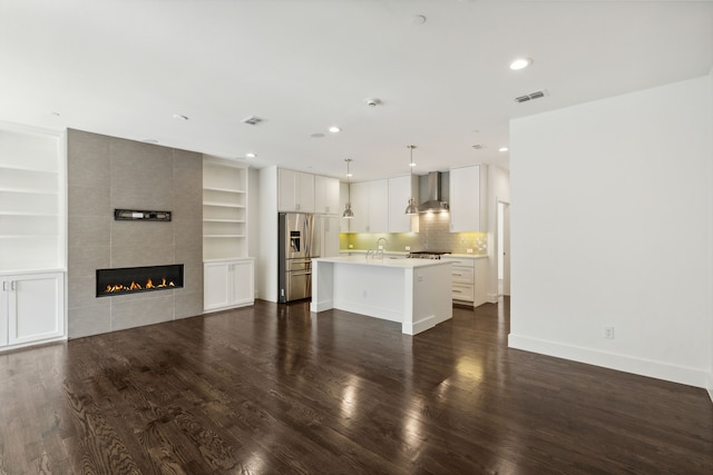 kitchen featuring built in features, a kitchen island with sink, dark hardwood / wood-style floors, wall chimney exhaust hood, and a tile fireplace