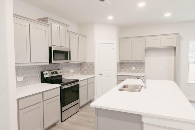 kitchen featuring light hardwood / wood-style floors, appliances with stainless steel finishes, a kitchen island with sink, sink, and backsplash