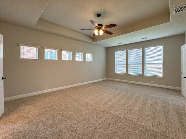 unfurnished room featuring a healthy amount of sunlight, ceiling fan, and a tray ceiling