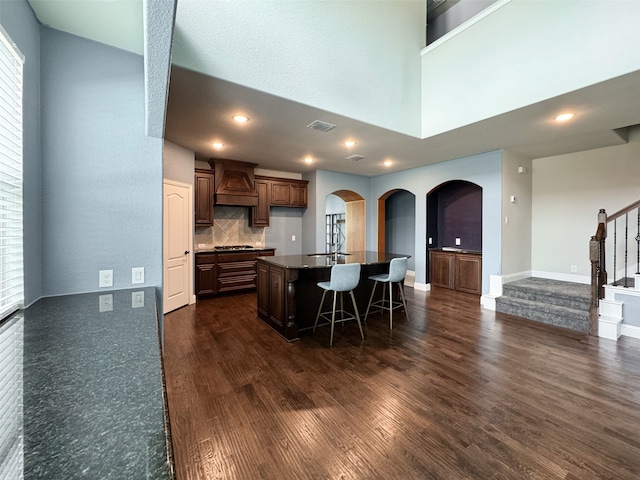 kitchen featuring tasteful backsplash, a kitchen bar, premium range hood, dark hardwood / wood-style floors, and a center island with sink