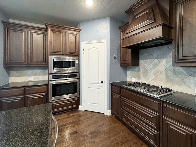 kitchen with custom exhaust hood, tasteful backsplash, a textured ceiling, dark wood-type flooring, and appliances with stainless steel finishes