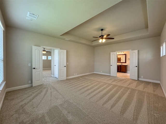 unfurnished room with a tray ceiling, ceiling fan, and light carpet