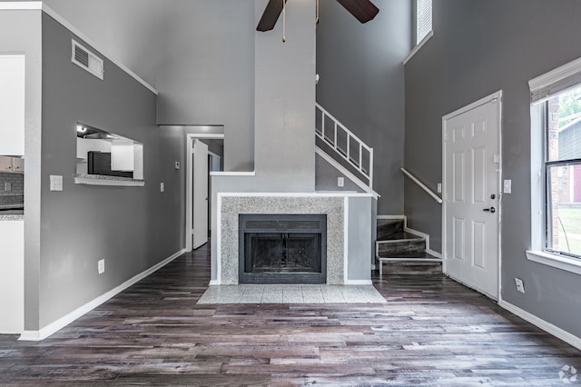 unfurnished living room with ceiling fan, a towering ceiling, dark hardwood / wood-style flooring, and a tiled fireplace