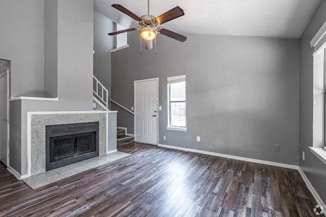 unfurnished living room with ceiling fan, dark hardwood / wood-style floors, a tiled fireplace, and high vaulted ceiling