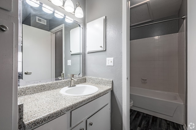 full bathroom with hardwood / wood-style flooring, tiled shower / bath, vanity, and toilet