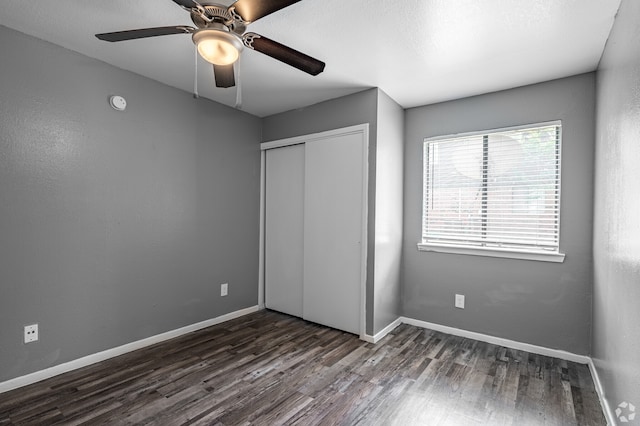 unfurnished bedroom with dark wood-type flooring, ceiling fan, and a closet