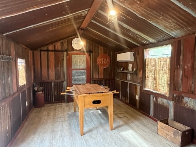 playroom with light hardwood / wood-style flooring, a wall mounted AC, wooden walls, and vaulted ceiling