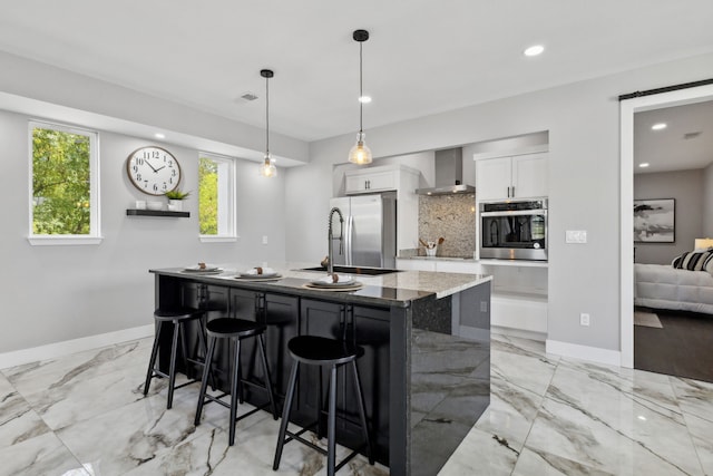 kitchen with stainless steel appliances, white cabinetry, decorative backsplash, wall chimney exhaust hood, and a kitchen bar